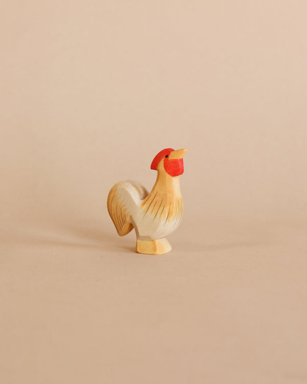 A Ostheimer Rooster - Ochre, painted in white and gold, stands against a plain, light tan background. The rooster is mid-strut with its head facing to the right, showcasing a