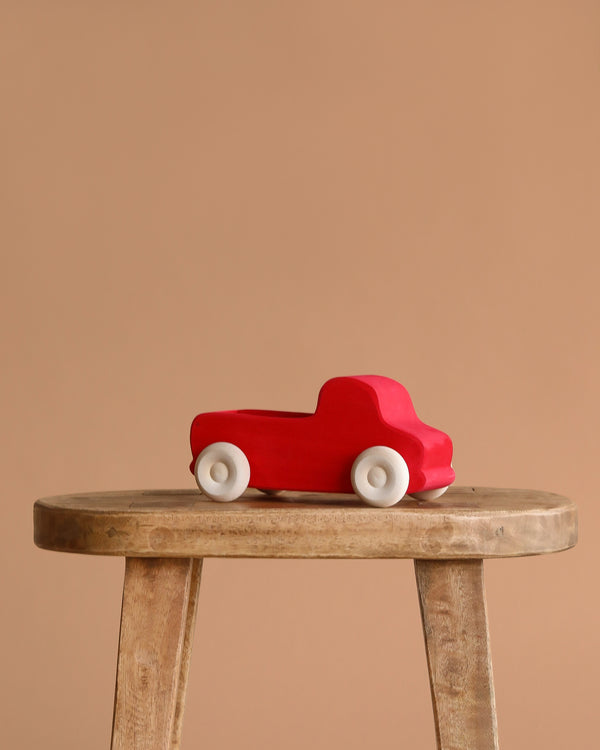 Grimm's Large Red Truck, made in Germany, with white wheels, is displayed on a wooden stool against a plain beige background.