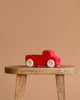 Grimm's Large Red Truck, made in Germany, with white wheels, is displayed on a wooden stool against a plain beige background.