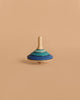 The Large Mader Tango Spinning Top - Dark Blue, crafted from maple wood with layered blue and teal rings, stands upright against a plain beige background, highlighting its safe design and elegant appearance.