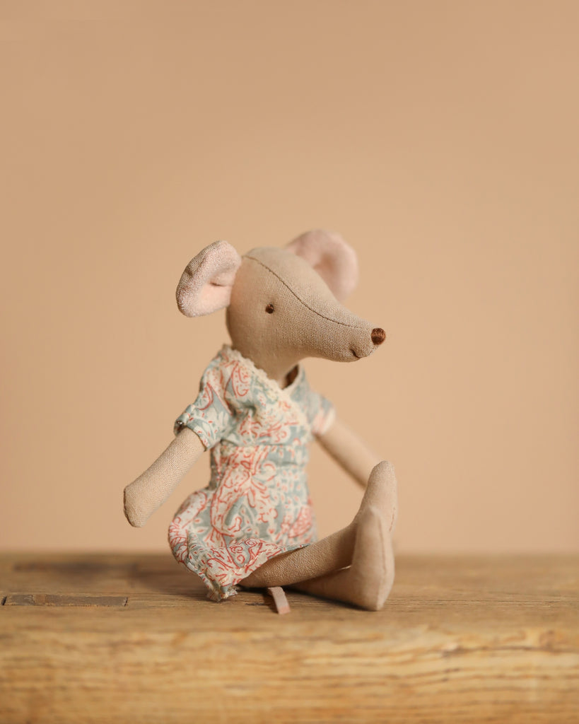 The Maileg Mom and Dad Living Room Set features a fabric mouse doll in a patterned dress seated by a charming tea set on a wooden surface, all set against a plain beige background.