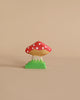 The Holztiger Handmade Wooden Animal Play Set features a small, decorative wooden mushroom with a red cap and white spots on a green base, showcasing European craftsmanship. Displayed against a plain beige background.