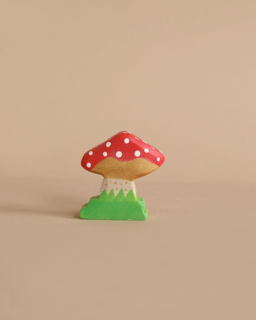 The Holztiger Handmade Wooden Animal Play Set features a small, decorative wooden mushroom with a red cap and white spots on a green base, showcasing European craftsmanship. Displayed against a plain beige background.