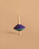 The Mader Tukanino Spinning Top - Purple, crafted from maple with a cream handle and purple, black, and green stripes, stands upright against a beige background, capturing the playful spirit of Austrian toys.