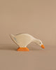 A Holztiger Goose, Feeding painted white with an orange beak and webbed feet is depicted against a plain beige background. The handcrafted wood toy, akin to HOLZTIGER figures, shows the goose in a bending position as if pecking at the ground.