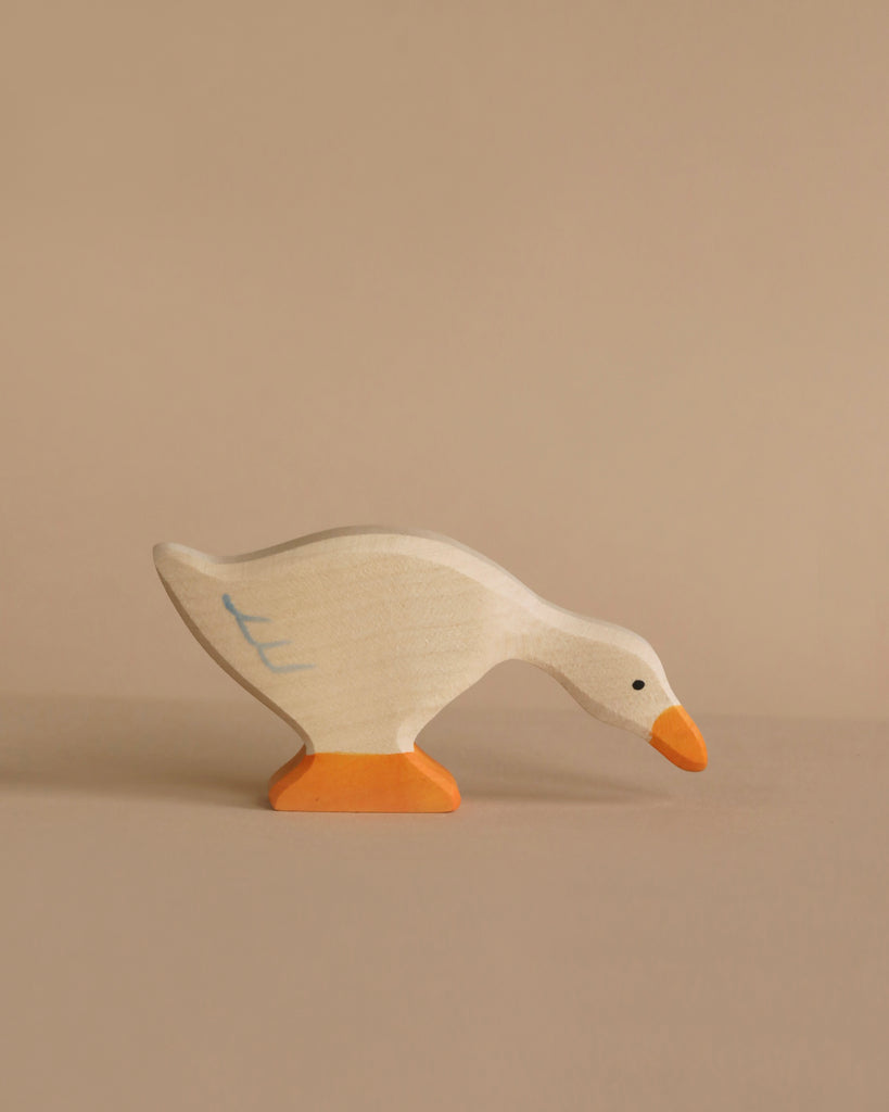 The Holztiger Handmade Wooden Woodland Animals Set includes a handcrafted wooden toy goose, painted white with orange beak and feet, standing on a beige surface. Inspired by HOLZTIGER figures, the goose looks downward—perfect for open-ended play.