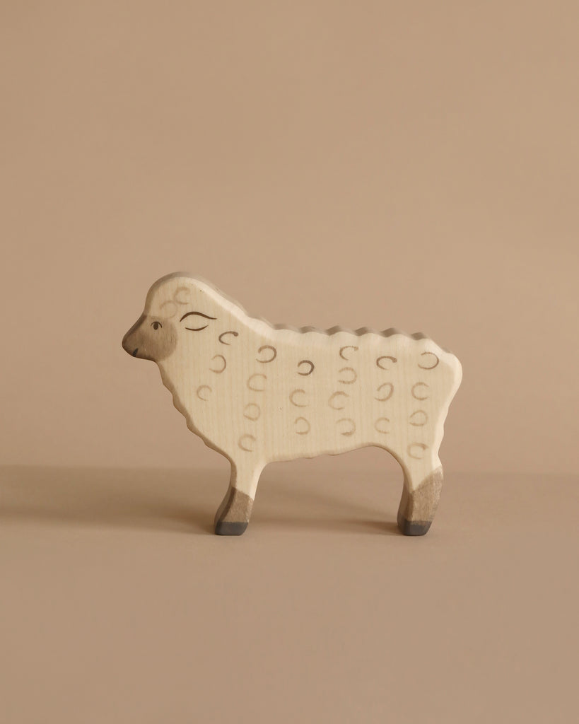 A wooden toy sheep with a natural finish and minimalistic design stands against a beige background. The handcrafted wood toy features simple engraved details to represent its wool and facial features, reminiscent of the quality found in Holztiger Sheep, Standing.