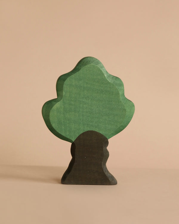 A minimalist wooden tree figurine with a green treetop and a brown trunk stands against a beige background. The softly rounded edges evoke a natural aesthetic, perfect for imaginative play often found in handcrafted Ostheimer Oak Tree toys.