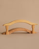 The Ostheimer Wooden Kingdom & Maileg Royal Family Set features a small, minimalist wooden bridge with smooth curves and two short legs, inspired by handcrafted toys, displayed on a neutral beige background.