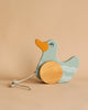 A wooden pull toy duck with mint green and natural milk paint, featuring large round wheels and a pull string, set against a plain, light brown background.