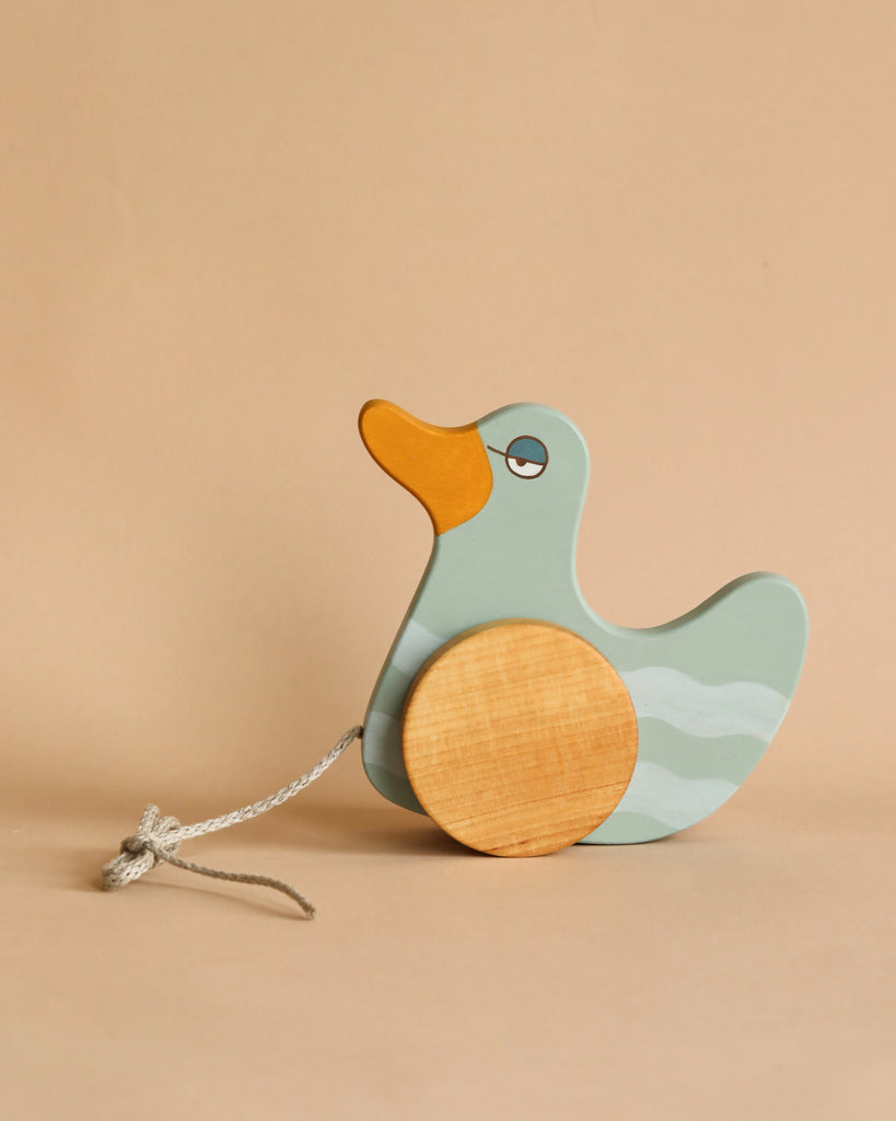 A wooden pull toy duck with mint green and natural milk paint, featuring large round wheels and a pull string, set against a plain, light brown background.