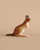 A handcrafted wooden figurine of a kangaroo, featuring detailed carving and a natural wood grain finish, stands against a plain, light brown background. Made from sustainable materials, the Ostheimer Kangaroo Father is depicted in a relaxed position with its tail extended behind it.