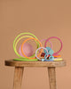 Grimm's Concentric Circles and Rings Building Set - Pastel features colorful wooden rings and discs of varying sizes, artfully stacked on a stool against a light brown backdrop, creating a playful and balanced display.