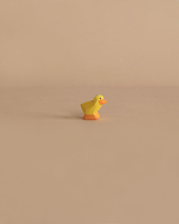 A small, yellow Ostheimer Chick with an orange beak is placed in the center of a beige background, creating a minimalistic composition that invites imaginative play.
