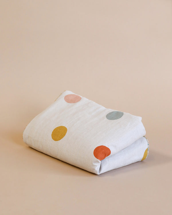 The Maileg Small Blanket - Rose features a neatly folded design made from linen fabric, adorned with large, vibrant polka dots in yellow, orange, blue, and pink against a classic beige background—ideal for introducing a playful element to any nursery.