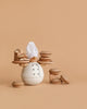 The Balance the Baker Stacking Game features a wooden chef with a white hat holding beechwood toy pastries and pies, surrounded by more pastries, all set against a plain beige background.