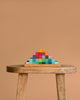 A wooden stool displays a neatly stacked pyramid of Grimm's Stepped Pyramid Block Set - Small against a plain beige background.