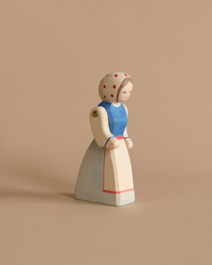 A handcrafted Ostheimer Farm Wife of a woman in a blue dress with a white apron and a headscarf adorned with red polka dots. Perfect for imaginative play, the figure features simple painted facial details and jointed arms, set against a plain beige background. Ideal for Ostheimer toys collectors.