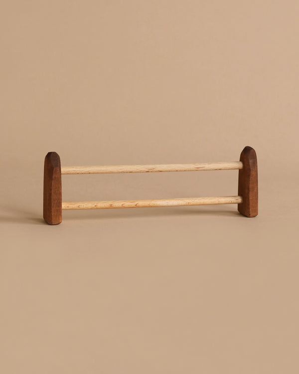 A minimalist wooden towel rack with two parallel rods and ends made of darker wood. The design echoes the handcrafted charm of the Ostheimer Fence, Small, set against a sandy beige background to create a cohesive and subtle aesthetic perfect for imaginative play in any space.