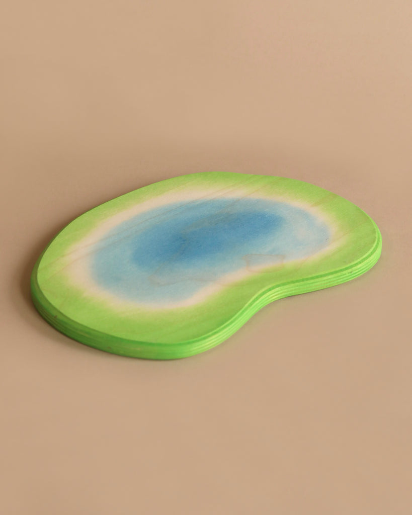 A stack of kidney-shaped coasters with a gradient design resembling a watercolor painting, featuring a green outer edge blending into a blue center. These Ostheimer Ponds are set against a simple beige background.