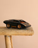The Playforeer UFO Cannone Car in Black, styled after 70's concept cars with gold accents, is displayed on a rustic wooden stool against a plain beige background.