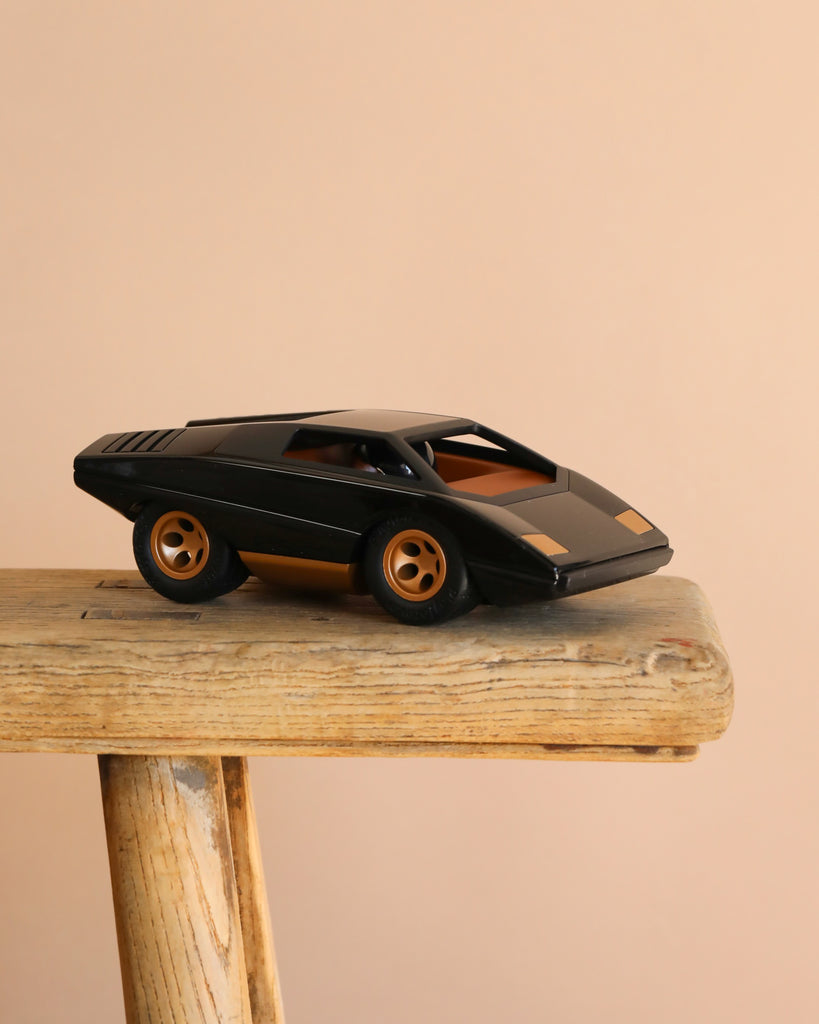 The Playforeer UFO Cannone Car in Black, styled after 70's concept cars with gold accents, is displayed on a rustic wooden stool against a plain beige background.