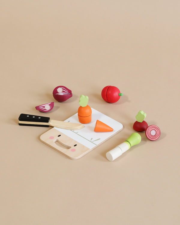A Mini Chef Chopping Board featuring a wooden chopping board, knife, and assorted vegetables like carrots, radishes, and onions, all on a beige background.