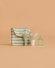 The Maileg LouiMax Bathroom Set, featuring a striped pouch with a small hairbrush, a toothbrush in a cup, a toothpaste tube, and a bottle labeled “FLORA,” is arranged neatly on a beige background—perfectly sized for your Maileg mouse to use alongside their Maileg sink dresser.