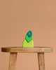 Three green Grimm's Tower Leaves Building Blocks—handpainted lime wood stones with white leaf symbols—are stacked on a wooden stool against a plain beige background.