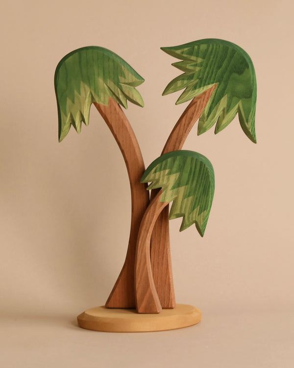 An Ostheimer Palm Trees With Stand of two stylized palm trees with green leaves on a tan, rounded base, standing against a plain beige background. The whimsical design features gently curving trunks and exaggerated, large leaves, perfect for imaginative play.