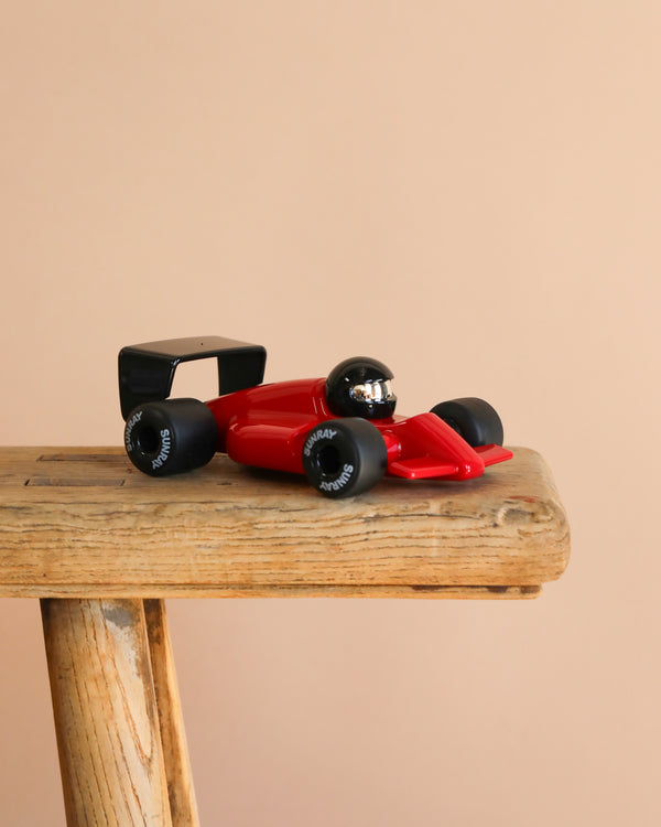 The Playforever Car TURBO Verve Laser Rich Red with black wheels and driver is placed on a rustic wooden stool against a plain beige background.