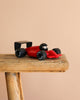 The Playforever Car TURBO Verve Laser Rich Red with black wheels and driver is placed on a rustic wooden stool against a plain beige background.