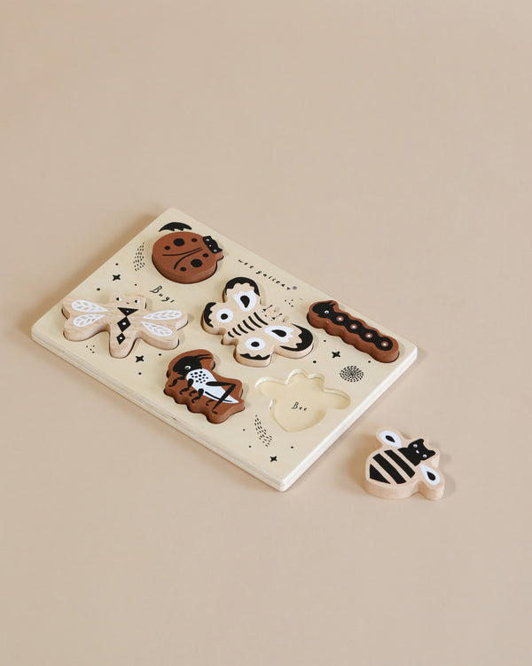 A ceramic plate with a variety of whimsical black and white cookies designed to resemble animals and abstract patterns, placed on a Wooden Tray Puzzle - Bugs.