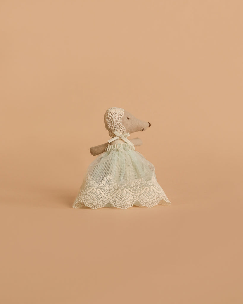The Maileg Baby Mouse in Gown - Mint stands upright, dressed in a mint celebration gown and lace bonnet, against a plain beige background.