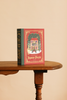 A rectangular Christmas Carols Jigsaw Puzzle 500-piece box featuring a red illustration of a house with Christmas decorations, sitting on a wooden table.