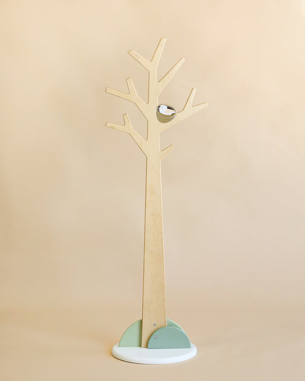 A minimalist wooden Forest Coat Stand with branches for hanging items, featuring a small circular mirror on one branch, set against a light beige background.