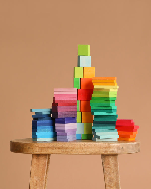 Grimm's Color Charts-Rally sits on a wooden stool, featuring vibrant blocks and tiles in different heights and shapes against a plain light brown background—ideal for developing fine motor skills.