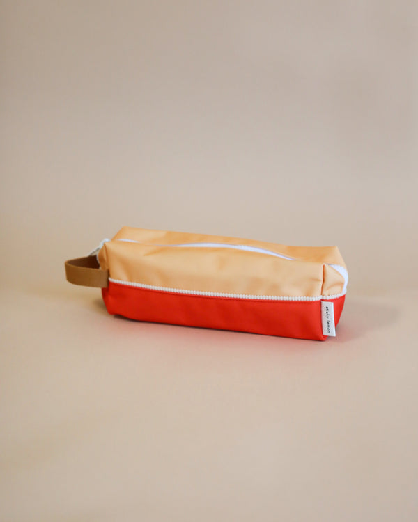 A Pear Jam + Ladybird Red pencil case with a YKK zipper, positioned horizontally on a tan background. The case has a small fabric tag visible on the side.