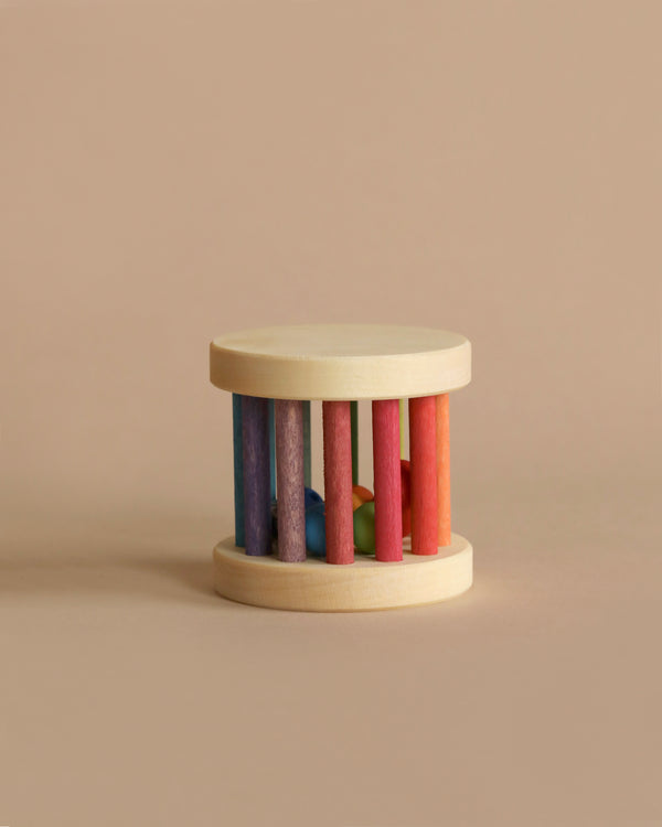 A Grimm's Mini Rolling Wheel with eight colorful vertical bars in red, pink, blue, purple, and green encircling its perimeter. The bars are attached to two round, natural wood bases on the top and bottom. Rolling like a wheel against a plain beige background, it also features wooden beads inside for added fun.