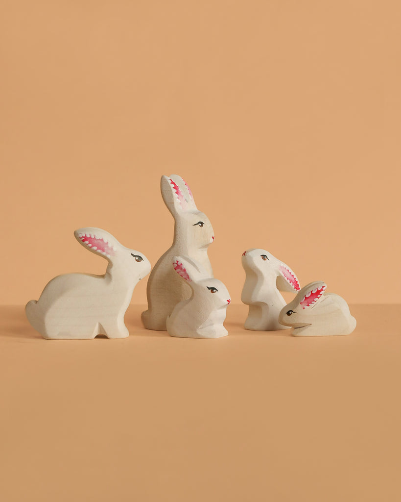 The Bumbu Handmade Wooden White Bunny Rabbit Family Set features four eco-friendly wooden rabbits with painted faces and pink ears, perfect for Montessori toy collections and beautifully arranged on a solid light orange background.