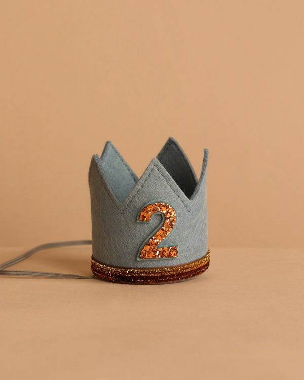 The Storm Gray Felt Crown features a glittery orange number 2 on the front and an orange glitter band around the base—perfect for birthday celebrations—shown against a beige background.