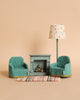 Maileg Living Room Starter Set with two teal armchairs, a blue cabinet with books, a colorful rug, and a lamp with a floral shade against a beige backdrop, designed as children's toys.