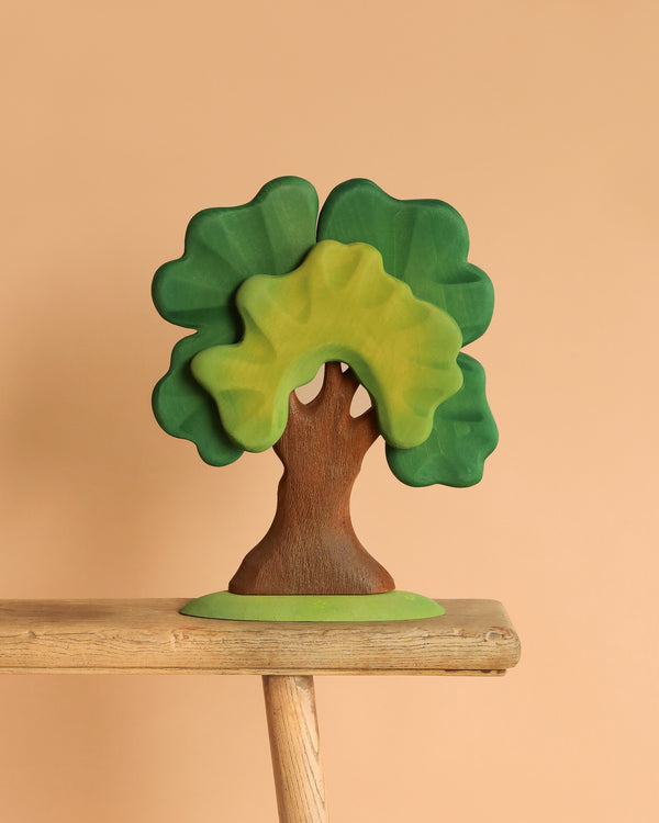 The Bumbu Handmade Wooden Extra Large Green Oak Tree features layered green leaves and a brown trunk. Perfect for imaginative play, this educational wooden toy stands on a light wood surface against a beige background.