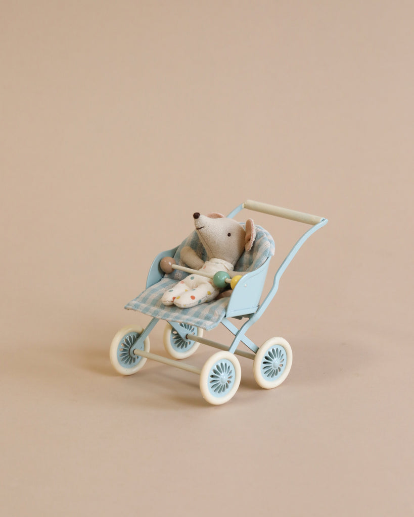 A small, stuffed toy mouse is seated in a Maileg Stroller, Baby Mice - Mint. The mouse, part of the tiny mouse families, is tucked in with a checkered blanket. The stroller, perfect to transport babies or toys alike, is set against a plain beige background.