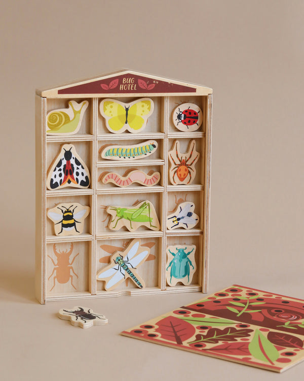 Sentence with product name: The Bug Hotel is a wooden educational toy shaped like a bug hotel with various colorful garden bug pieces slotted into matched compartments, and a puzzle piece on the side, placed on a light beige background.