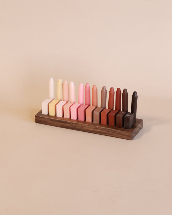 A Wooden Crayon Holder 12 Stick / 12 Block Slots made in the USA displays a collection of colorful wax crayons arranged in a gradient from light to dark tones against a neutral background.