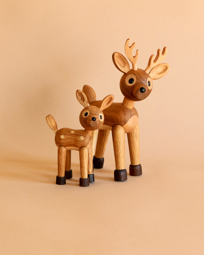 Two Spring Copenhagen Spot The Fawn figurines with a larger FSC Oak deer standing next to a smaller deer calf figure, both with spotted bodies and dark hooves, on a solid beige background.