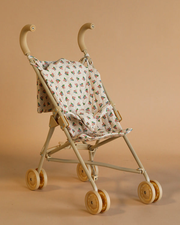 The Konges Sloejd Doll Stroller - Verona Blues is a lightweight stroller with curved handles, four sets of double tan wheels, and a removable floral-patterned fabric seat, shown against a plain tan background.
