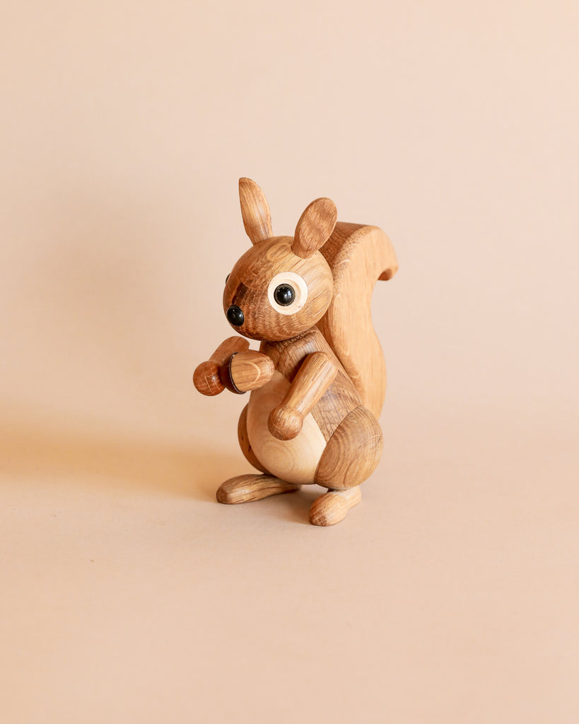A Spring Copenhagen Hazel figurine with large, cartoonish eyes, standing upright and holding an acorn, set against a plain beige background.