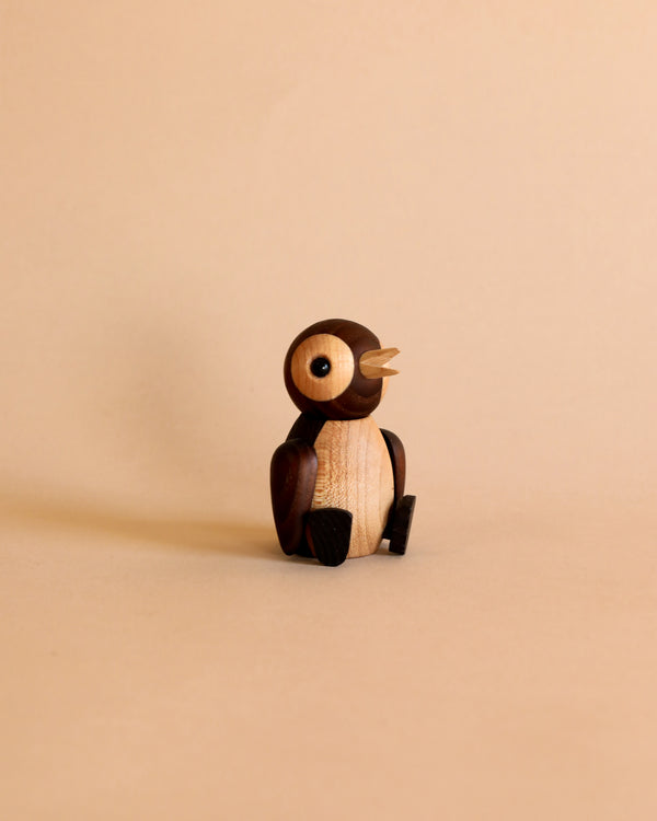 A small, wooden Spring Copenhagen Snow figurine with intricate detailing stands against a plain beige background. This handmade wooden decoration features lighter FSC thermo ash for its face and darker wood for its body and eyes.